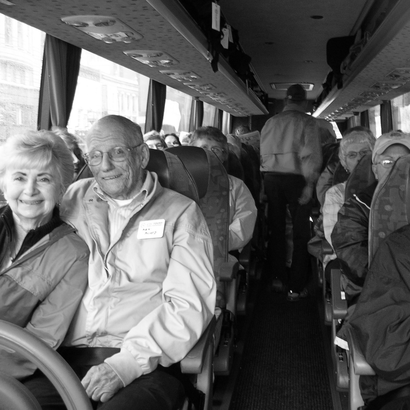A smiling older couple sit close together on a bus